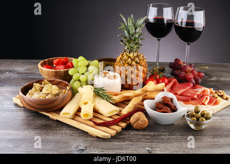 Vin antipasti italiens des en-cas. Variété de fromage, olives, cornichons, Méditerranée jambon de Parme au melon, vin au verre sur fond noir grunge ba Banque D'Images