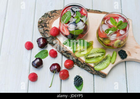 Verres de l'eau de fruits avec divers ingrédients présentés sur un arbre dur Banque D'Images