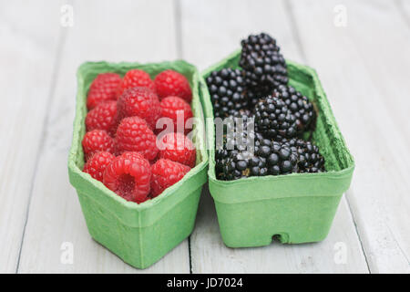 Les framboises et les mûres dans une boîte en carton sur une planche de bois blanc Banque D'Images