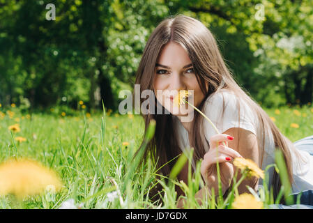 Belle jeune femme portant sur l'herbe avec des fleurs de pissenlit dans park Banque D'Images
