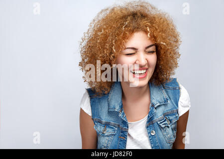 Portrait of beautiful happy mixed race girl bouclés en style casual rit. looking at camera. studio shot sur fond gris clair. Banque D'Images