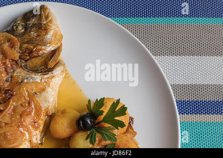 Le poisson cuit au four, accompagné de pommes de terre à l'or et les olives dans un plat blanc. Plat typiquement portugaise. Banque D'Images