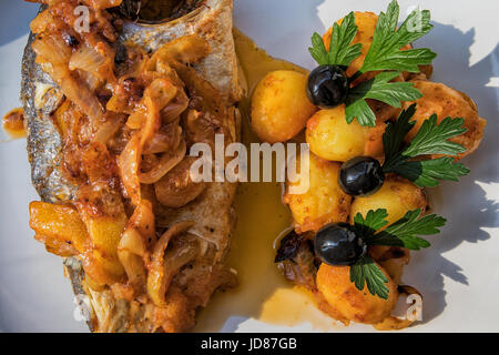 Le poisson cuit au four, accompagné de pommes de terre à l'or et les olives dans un plat blanc. Plat typiquement portugaise. Banque D'Images