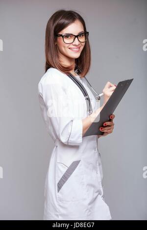 Portrait d'une jolie jeune femme médecin ou infirmière portant des lunettes en uniforme blanc avec des documents médicaux holding stethoscope Banque D'Images