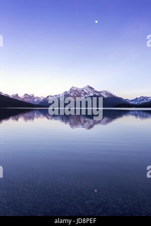 Pleine lune au-dessus de l'eau calme du lac maligne. Ciel nocturne Portrait horizon paysage des montagnes Rocheuses. Parc national Jasper randonnée Rocheuses canadiennes Alberta Banque D'Images