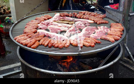 Un vendeur de rue de cuisiniers et de dalles de saucisses de porc sur un grand barbecue Banque D'Images