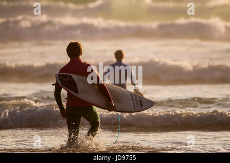 Quelques surfeurs dans la mer au coucher du soleil. La plage de Fistral, Newquay, Cornwall. Banque D'Images