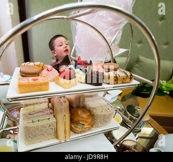 Jeune garçon ayant le thé l'après-midi dans un restaurant avec des gâteaux et des sandwichs on cake stand, Close up. 2016 urban city United States of America Banque D'Images