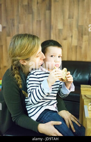 Jeune garçon assis sur les genoux de sa mère, boy eating sandwich, looking at camera Banque D'Images