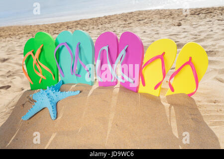 Été plage fun - jeu de famille - sandales de couleur vert, bleu, rose et jaune - dans le sable sur la plage de Las Teresitas, Tenerife, Canarias Banque D'Images