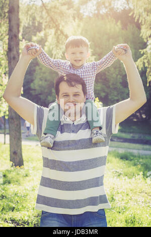 Heureux père et son fils âgé de deux ans sur les épaules de papa dans le parc au coucher du soleil Banque D'Images