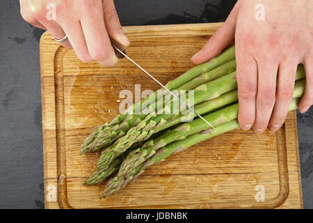 Femme coupe les mains lavées avec asperges vertes fraîches sur couteau planche à découper en bois des gouttes d'eau, Close up, augmentation de la vue supérieure Banque D'Images