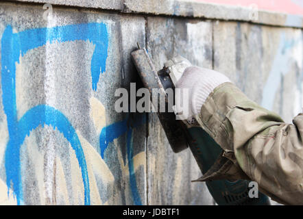 L'enlèvement de graffiti sur un mur de béton d'un passage souterrain à l'aide d'une meule d'angle Banque D'Images