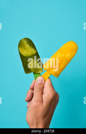 Libre d'un jeune homme de race blanche avec deux différents produits naturels faits ice pop dans sa main, contre un fond bleu lumineux Banque D'Images