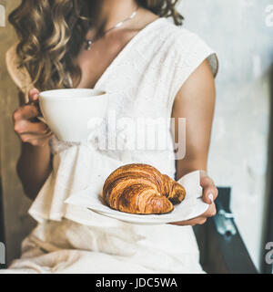 Blond woman holding croissant et cappuccino au café, récolte carrés Banque D'Images