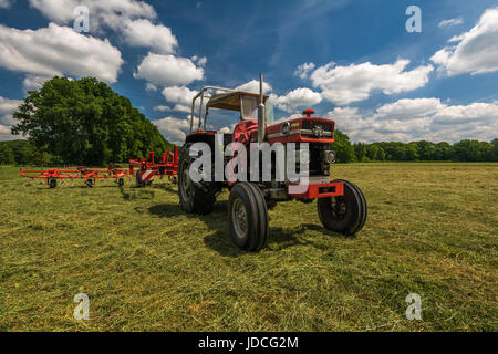 Un tracteur avec une faneuse debout sur un champ après fanage l'herbe pour la préparation de foin sur une chaude journée d'été aux Pays-Bas Banque D'Images