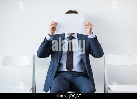 Woman covering face avec papier alors qu'assis sur une chaise Banque D'Images