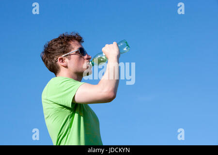 Jeune homme de l'eau potable en bouteille t shirt vert contre fond bleu clair Banque D'Images
