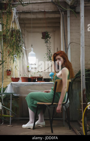 Belle jeune fille rousse en robe verte à regarder parmi les plantes nature Banque D'Images