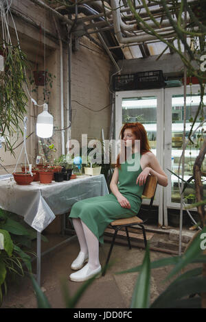 Belle jeune fille rousse en robe verte à contempler dans la verdure de la lampe entre les plantes Banque D'Images