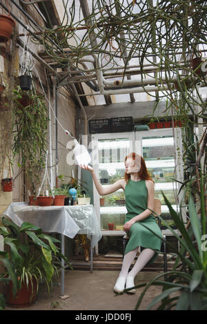 Rousse pensive fille assise près de table dans la verdure et à la lampe à Banque D'Images