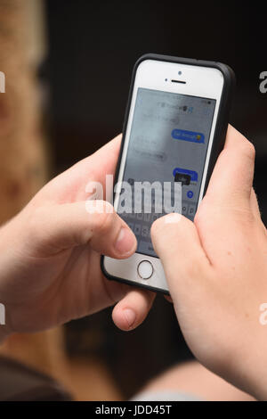 Close Up of Teenage boy âgés de 19 ans en utilisant un iPhone d'Apple se téléphone mobile pour lire et envoyer des messages texte Banque D'Images