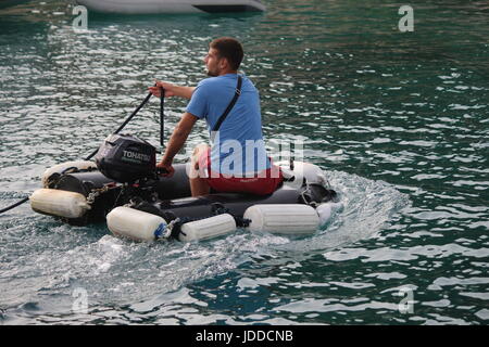 L'homme en T-shirt bleu petite manoeuvre canot rond comme bateau avec flotteurs blanc attaché, tout en aidant à amarrer les bateaux Banque D'Images