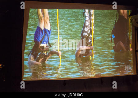 Merrick, New York, USA. 11 Juin, 2017. Au cours de la saison 2 de grain américain, première à gauche en maillot bleu, CHRIS Édom, 48 ans, de Merrick, est suspendu à l'envers avec sa tête sous l'eau comme lui et d'autres concurrents sont abaissés dans le lac lors d'un défi. Spectacle a été projeté sur grand écran au cours de l'arrière-cour d'Edom Partie Visualisation pour l'épisode 1 de l'émission de télé-réalité du réseau FOX. Édom a été mise de 16 candidats sélectionnés pour une équipe que l'épisode. Credit : Ann Parry/ZUMA/Alamy Fil Live News Banque D'Images