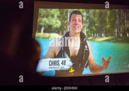 Merrick, New York, USA. 11 Juin, 2017. CHRIS Édom, grain américain, candidat à la télévision, 48 de Merrick, NY, parle dans la scène projetée sur grand écran de télévision dat Affichage d'arrière-cour fête organisée par la famille d'Édom, en cours de diffusion de la saison 2 de la première émission de télé-réalité du réseau FOX. Édom a été mise de 16 participants choisis pour l'une des 4 équipes. Credit : Ann Parry/ZUMA/Alamy Fil Live News Banque D'Images