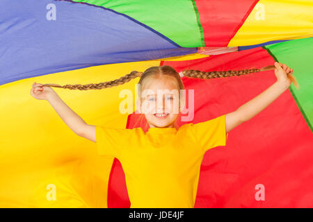 Jolie petite fille avec deux tresses debout sous la tente faite de parachute coloré Banque D'Images