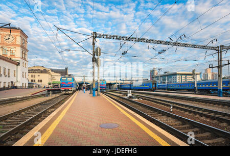 Gare avec des trains bleu au coucher du soleil en été en Europe. Paysage avec chemin de fer, les trains de passagers, ciel bleu avec des nuages dans le même Banque D'Images