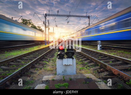 Les trains de voyageurs à grande vitesse en mouvement sur la voie de chemin de fer au coucher du soleil. Avec la gare de train de banlieue moderne brouillée, feu de circulation ferroviaire, bleu clo Banque D'Images