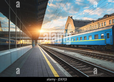 Belle blue train de voyageurs à la gare au coucher du soleil. Vue industrielle moderne, avec la plate-forme ferroviaire, chemin de fer, bâtiments et ciel bleu Banque D'Images