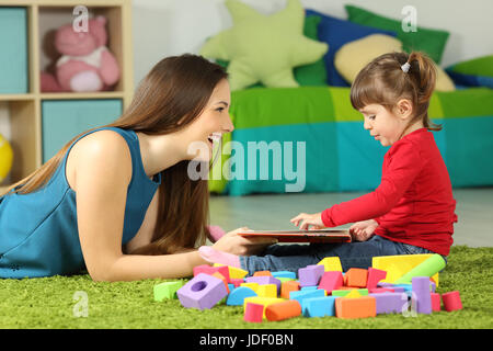 Vue latérale d'une mère et d'enfant en jouant avec un livre assis sur un tapis dans la chambre à coucher à la maison Banque D'Images