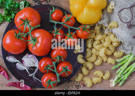 Ingrédients pour la cuisine italienne - pâtes italiennes et les légumes crus, différentes variétés de tomates, l'ail, les asperges, le poivron sur fond de bois. Vue d'en haut Banque D'Images