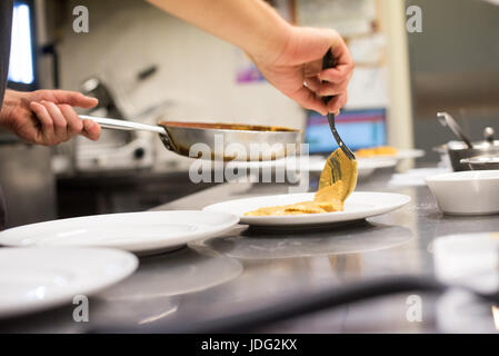 Le chef sert des pâtes italiennes faites et cuits dans une cuisine de restaurant cuillerées sur une assiette avec la sauce de la poêle dans une vie Banque D'Images