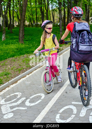 Chemin de bicyclette pour enfant filles portant casque avec sac à dos en ciclyng. Les enfants sont sur la voie cyclable blanc. Alternative aux transports urbains. La circulation en sens inverse. Banque D'Images