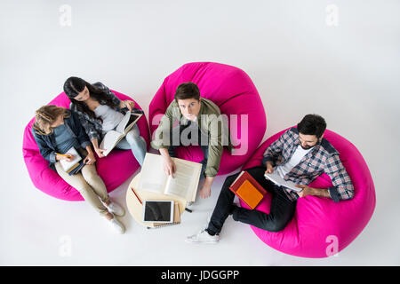 Vue aérienne d'étudiants assis sur des chaises de pouf et d'étudier en studio sur fond blanc Banque D'Images