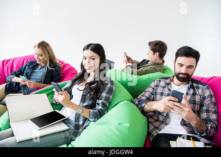 Les élèves assis sur des chaises de pouf et d'étudier et d'utiliser les smartphones en studio sur fond blanc Banque D'Images