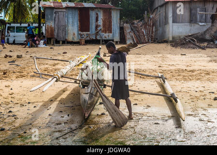 Ambatozavavy, Nosy Be, Madagascar - Le 19 décembre 2015 : batelier et sa pirogue en bois traditionnel avec outrigger dans le village de pêche Ambatozavavy sur Banque D'Images