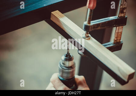 L'homme à l'aide de la perceuse fait un trou dans le bois et fer à repasser. le processus de fabrication de meubles de bureau,. soft focus dof. peu profondes. Banque D'Images