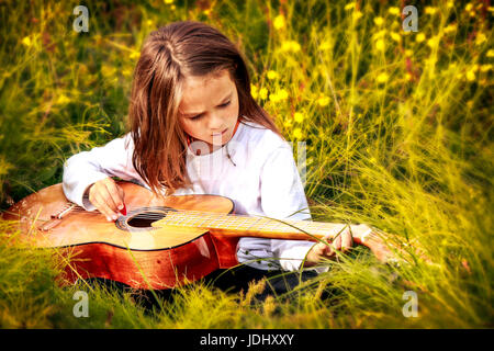 Enfant assis dans l'herbe en jouant de la guitare Banque D'Images