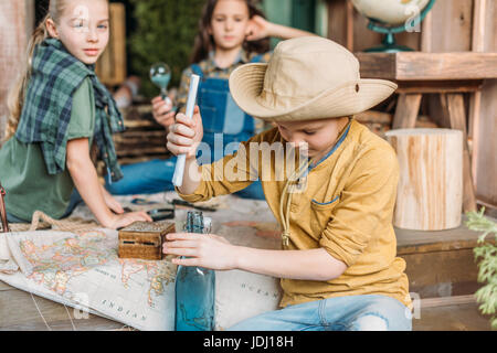 Boy putting message dans une bouteille, deux filles avec la carte derrière le porche, cute kids concept Banque D'Images