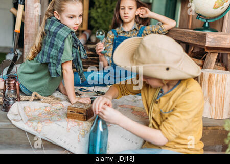 Boy putting message dans une bouteille, deux filles avec la carte derrière le porche, cute kids concept Banque D'Images