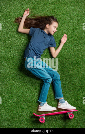 Vue de dessus de cute little Girl with pink skateboard allongé sur pelouse verte Banque D'Images