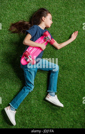 Vue de dessus de cute little Girl with pink skateboard allongé sur pelouse verte Banque D'Images