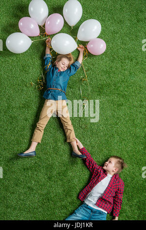 Vue de dessus de little boy holding smiling girl with balloons on grass Banque D'Images