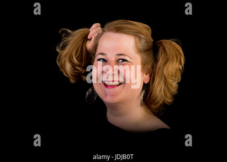 Aux cheveux rouge attrayant embonpoint lite femme mature européenne avec drôle de cheveux - tirant ses cheveux, studio shot sur fond sombre Banque D'Images