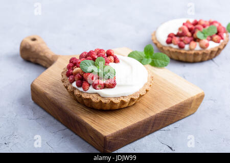 Tartelettes aux fraises sauvages avec la crème, de délicieux fruits d'été mini tartelettes sur planche à découper rustique Banque D'Images