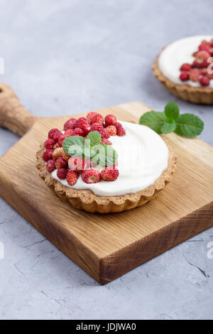 Tartelettes aux fraises sauvages avec la crème, de délicieux fruits d'été mini tartelettes sur planche à découper rustique Banque D'Images